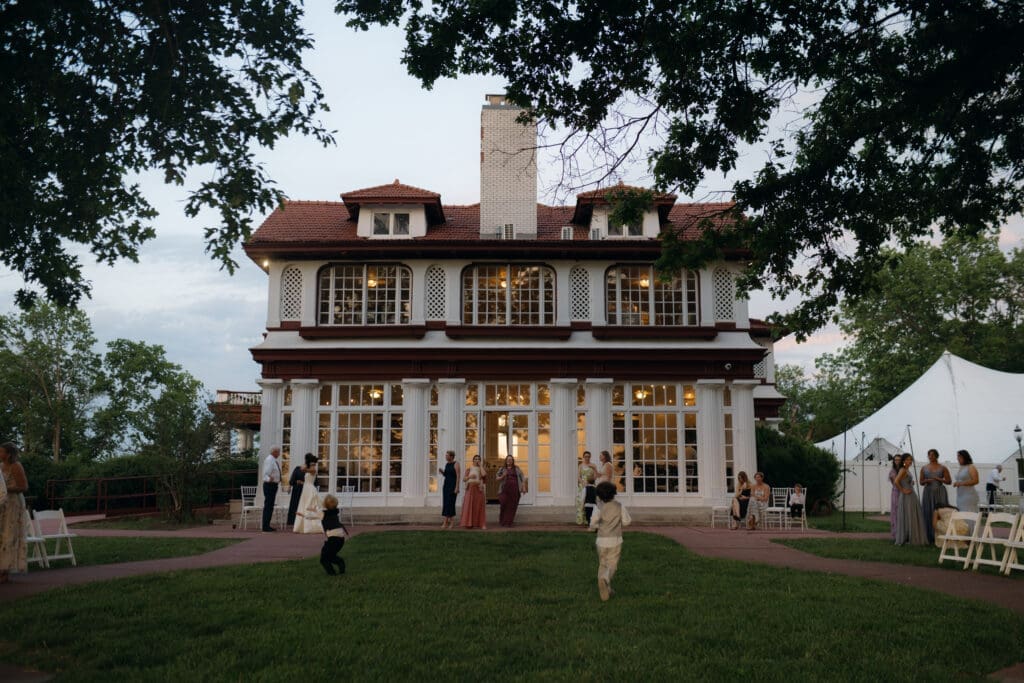 Candid sunset photography of wedding guests socializing on the lawn by the side of the historic Longview Mansion during golden hour.
