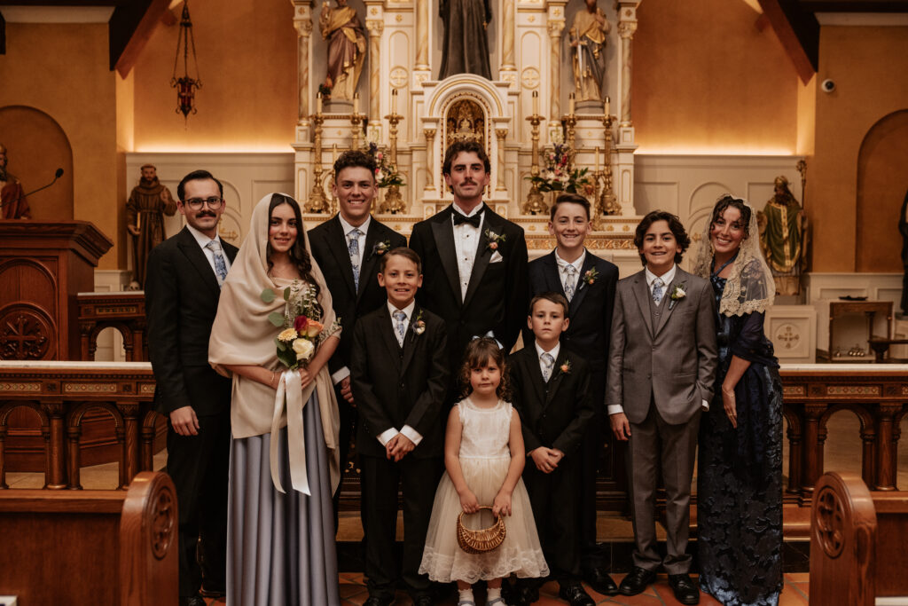 Wedding party portrait at St. Rose Philippine Duchesne featuring the groom, bridesmaids wearing lace mantilla veils, and young groomsmen in dark suits.