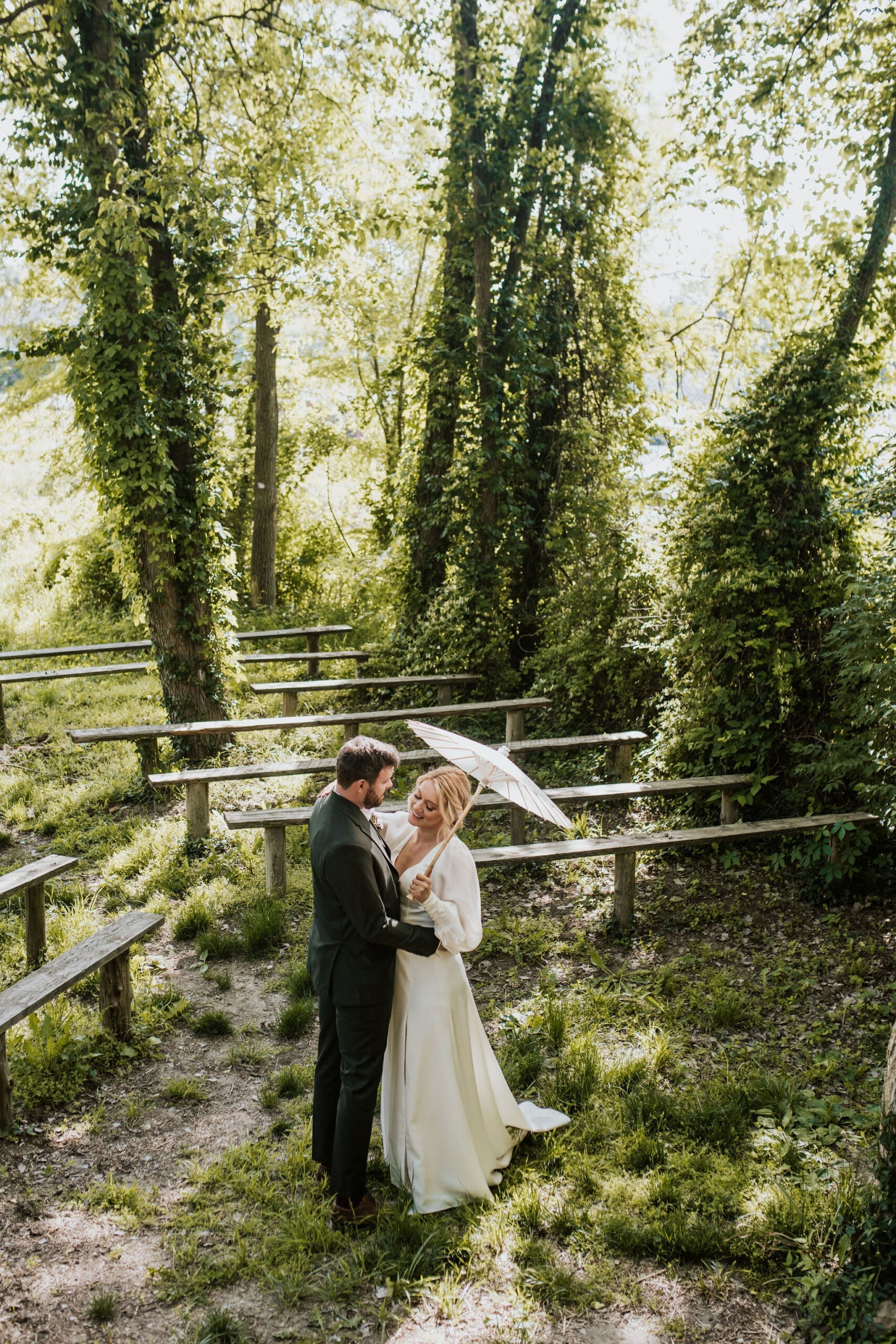 a bride with a parasol stands with a groom in a spring forest in weston missouri