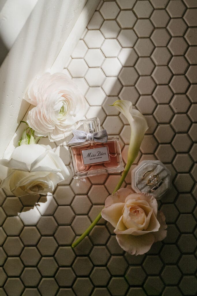 Bridal getting-ready details with perfume, ring box, and roses on hexagon tile