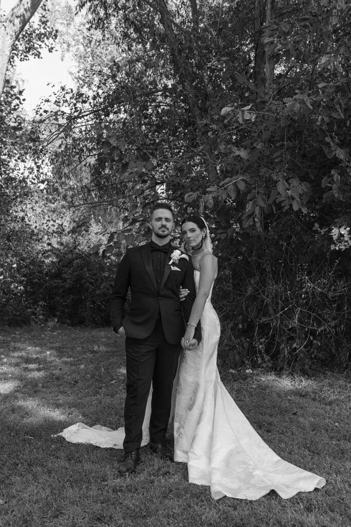 Black and white portrait of bride and groom standing together under trees