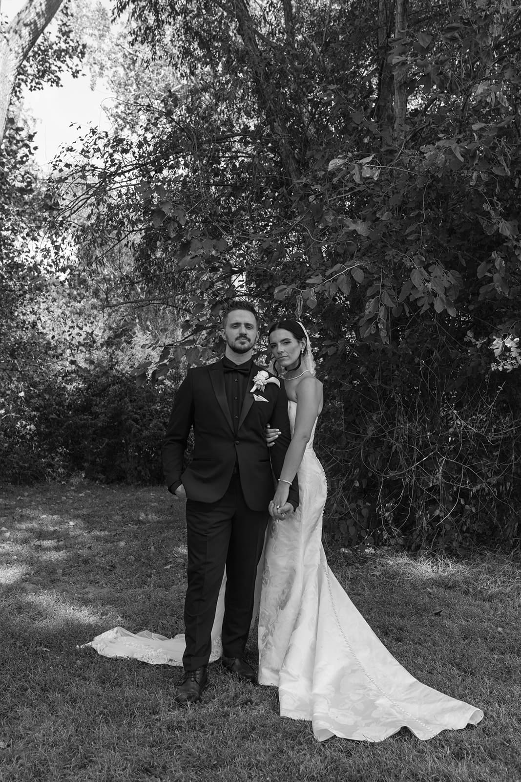 Black and white portrait of bride and groom standing together under trees