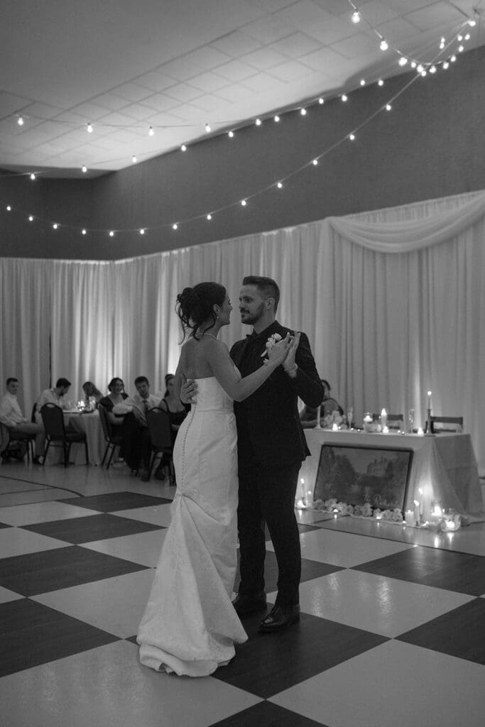 Black and white photo of bride and groom's first dance on a checkered dance floor
