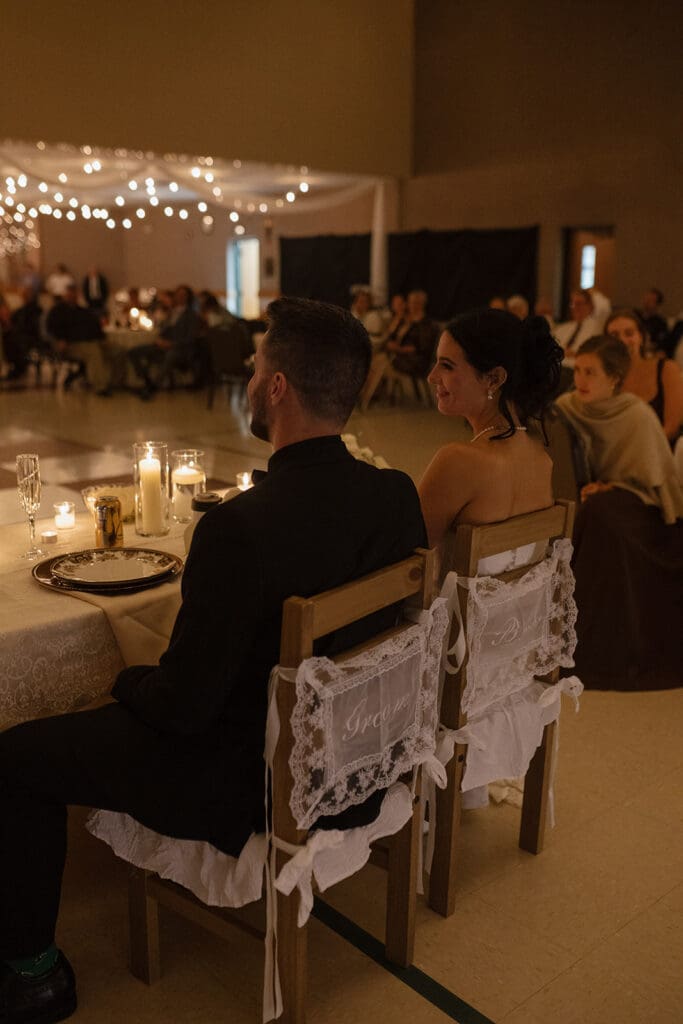 Bride and groom seated at their reception table with lace 'Bride' and 'Groom' chair signs