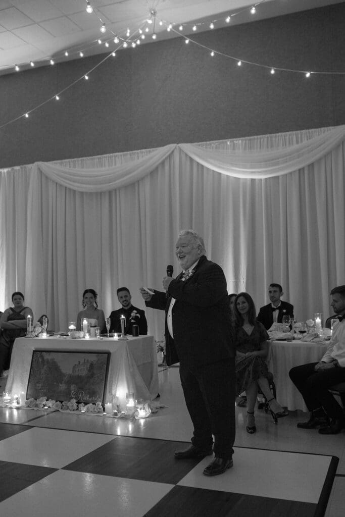 Black and white photo of a wedding guest giving a speech at the reception