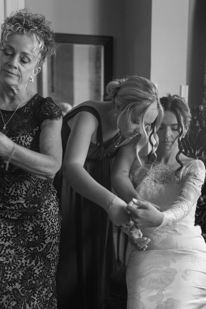 Black and white photo of bride getting help into her dress from her mother and sister