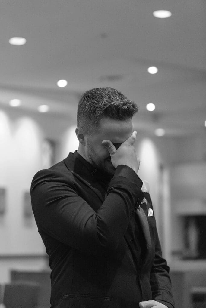 Black and white photo of groom wiping away tears before the wedding ceremony
