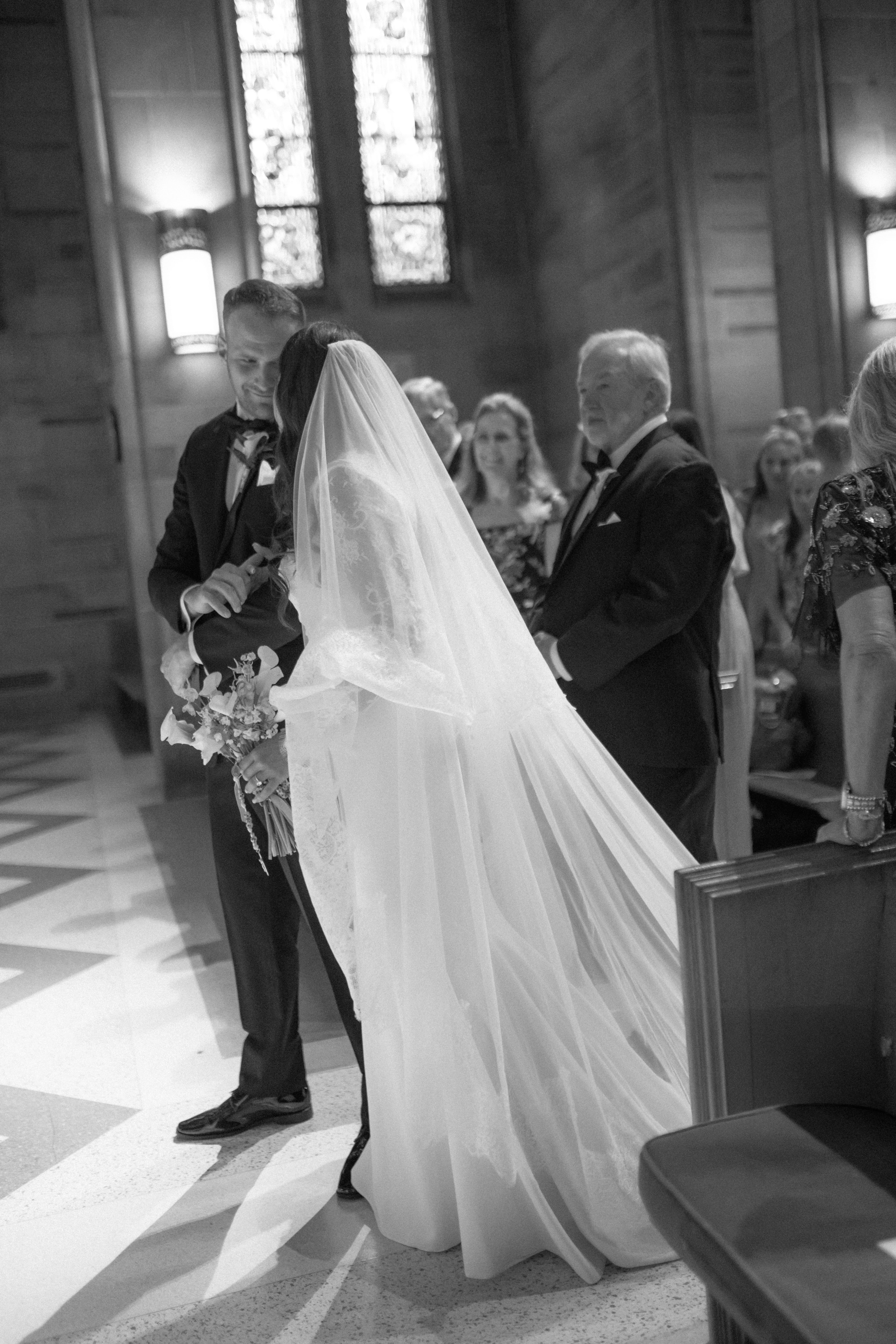 a black and white image of a bride and groom meeting at the altar on their catholic wedding day
